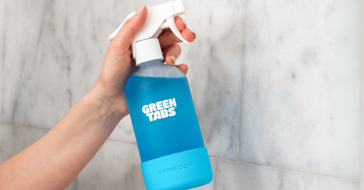 bathroom spray greentabs in glass foever bottle being held in hand and spray on bathroom tiles