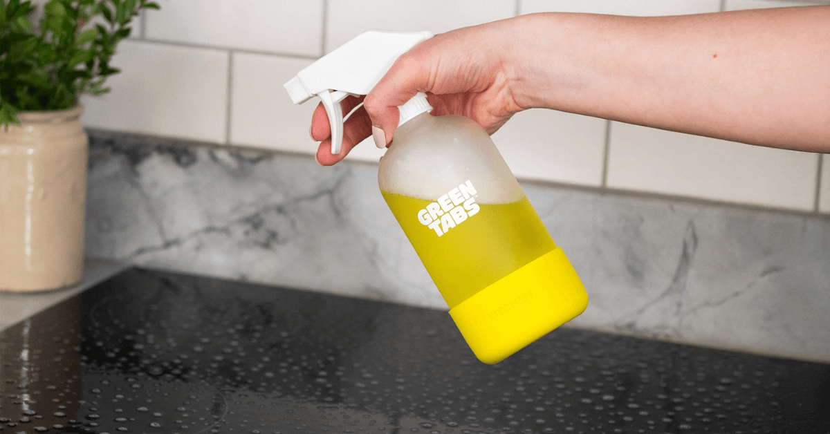 eco-friendly kitchen degreaser in glass bottle being sprayed on hob