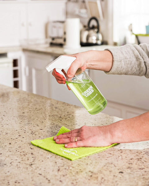 Lifestyle image of a hand cleaning and spraying a clean kitchen worktop with multipurpose GreenTabs spray in green, filled in a reusable bottle