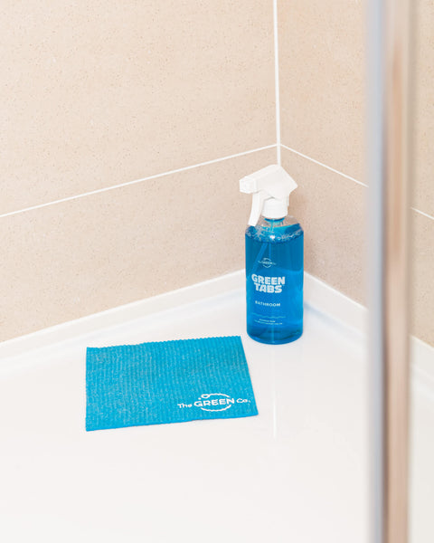 Blue bathroom cleaner in a reusable bottle standing on a shower floor wet wall with a blue cellulose dish cloth