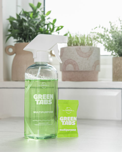 Green multipurpose cleaner in reusable bottle with the multipurpose GreenTab standing in front of the bottle about to be used to clean inside kitchen cupboards