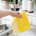 Yellow Cellulose Dish Cloth dripping of soapy water, being held over filled sink with bubbled in a kitchen environment