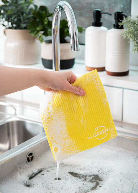 Yellow Cellulose Dish Cloth dripping of soapy water, being held over filled sink with bubbled in a kitchen environment