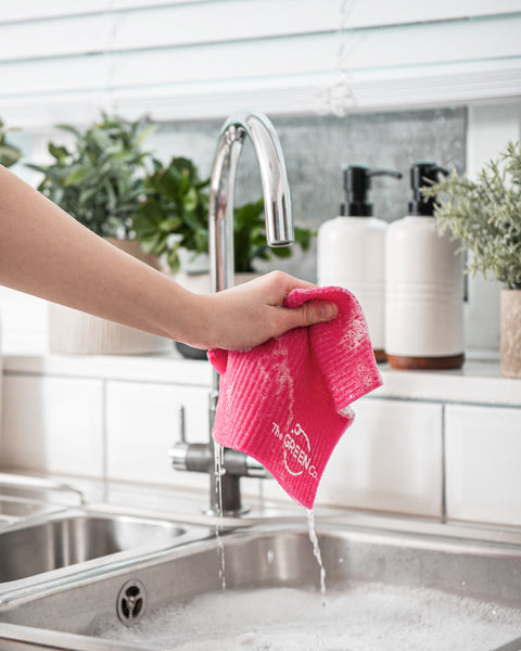 Pink Cellulose Dish Cloth dripping of soapy water and being wrung out and held over filled sink with bubbled in a kitchen environment