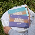 Blue Fresh Linen Fabric conditioner GreenSheets and Purple Lavender Fabric conditioner GreenSheets in a laundry basket outside infront of a hedge