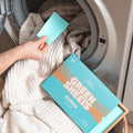 Blue Fresh Linen Fabric conditioner GreenSheets getting put into the washing machine. Packaging lying on top of washing basket with laundry