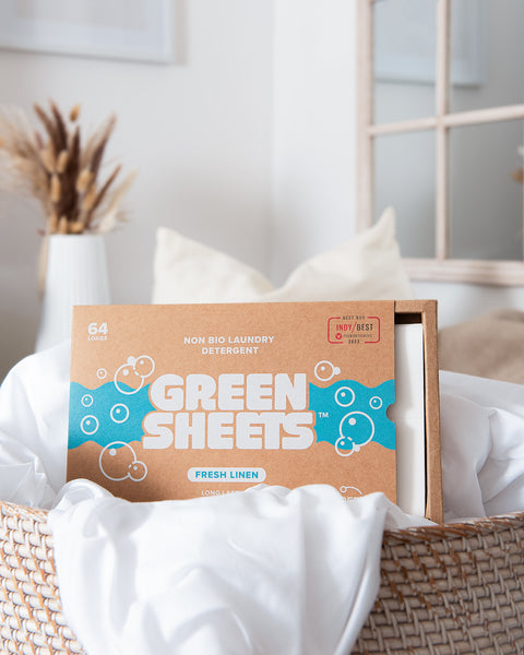 Green Company laundry strips fresh linen 64 pack sitting in a wicker laundry basket with white bed linen