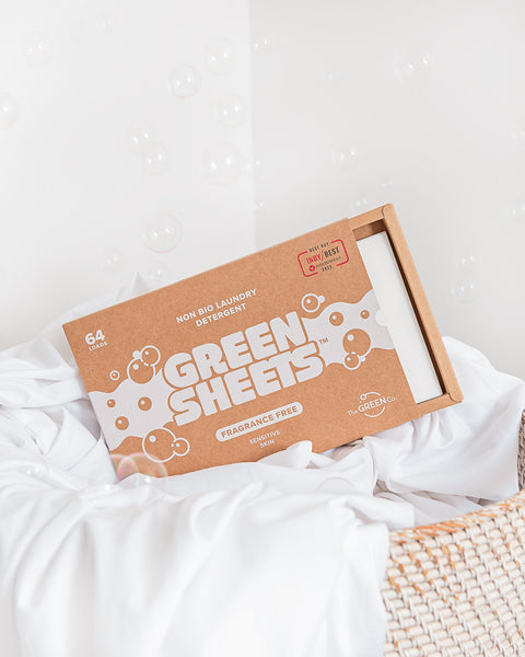 The Green Company unscented laundry detergent 64 load pack sitting in a wicker laundry basket with some clean, white bed linen