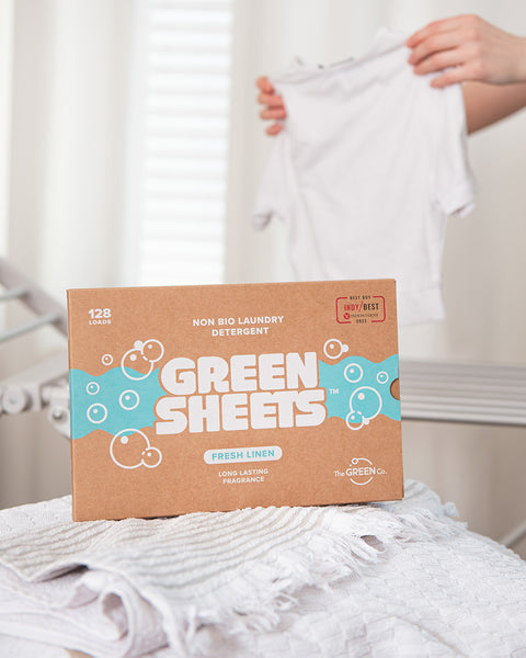 The Green Company fresh linen non bio laundry detergent 128 load pack resting on a white towel, next to some white t shirts being folded after a wash