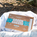 the green company vegan laundry detergent sheets, fresh linen 64 load pack outside in a washing basket, resting on 3 white towels