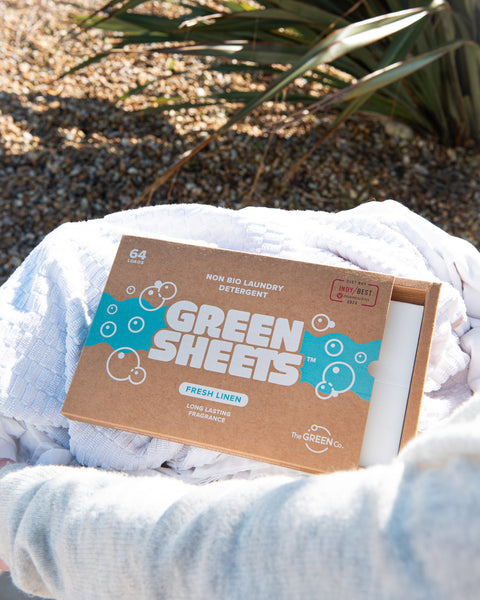 the green company vegan laundry detergent sheets, fresh linen 64 load pack outside in a washing basket, resting on 3 white towels