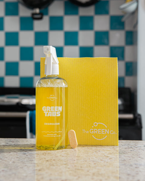 yellow kitchen degreaser GreenTab in forever bottle with yellow GreenTab and yellow cellulose dish cloth, sitting on kitchen worktop in front of blue and white kitchen tiles