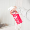 Hand holding pink Glass Cleaner GreenTab in forever bottle against a mirror