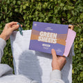 Lavender Fabric conditioner GreenSheets being held up whilst hanging up fresh laundry on a clothing line in a garden setting