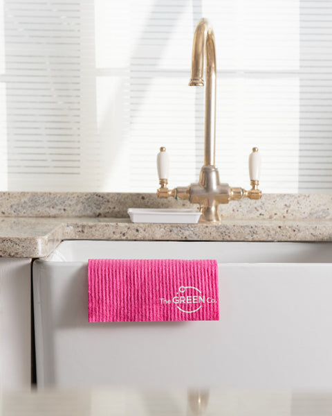 Pink Cellulose Dish Cloth hanging over the edge of a ceramic sink with golden tap