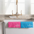 Pink Cellulose Dish Cloth and Blue  Cellulose Dish Cloth hanging over the edge of a ceramic sink with golden tap